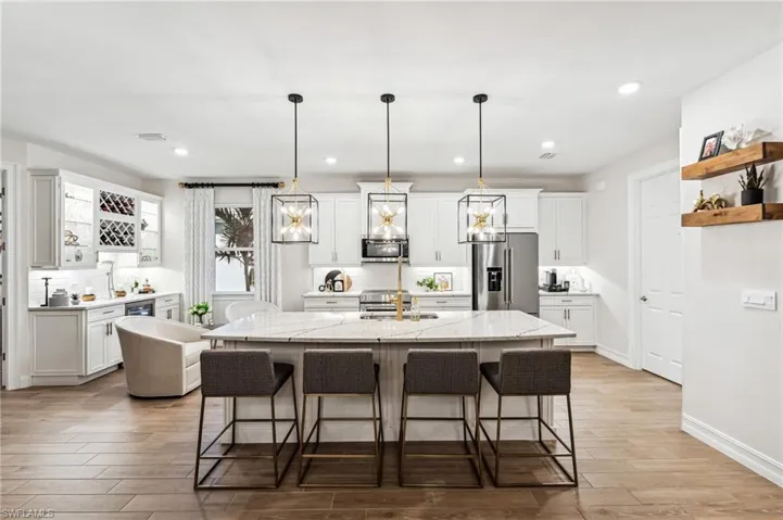 Kitchen featuring light stone countertops, stainless steel appliances, a kitchen island with sink, and hanging light fixtures