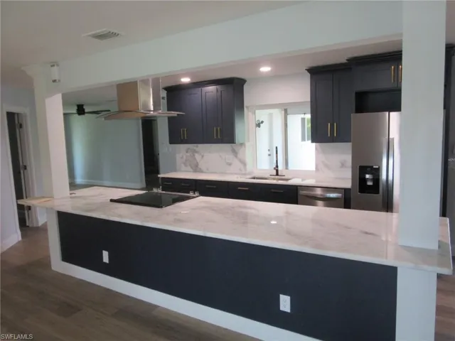 Kitchen featuring stainless steel appliances, light stone countertops, dark wood finished floors, exhaust hood, and backsplash