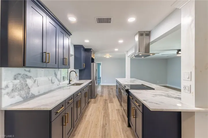 Kitchen featuring light stone countertops, electric range oven, recessed lighting, island range hood, and light wood finished floors