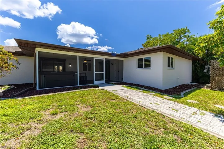 Rear view of property with a yard, stucco siding, a sunroom, and a ceiling fan