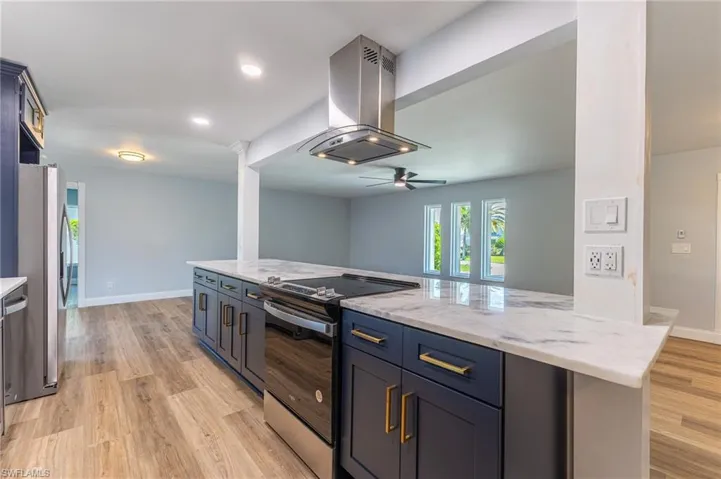 Kitchen featuring electric range, light stone counters, island range hood, freestanding refrigerator, and blue cabinetry
