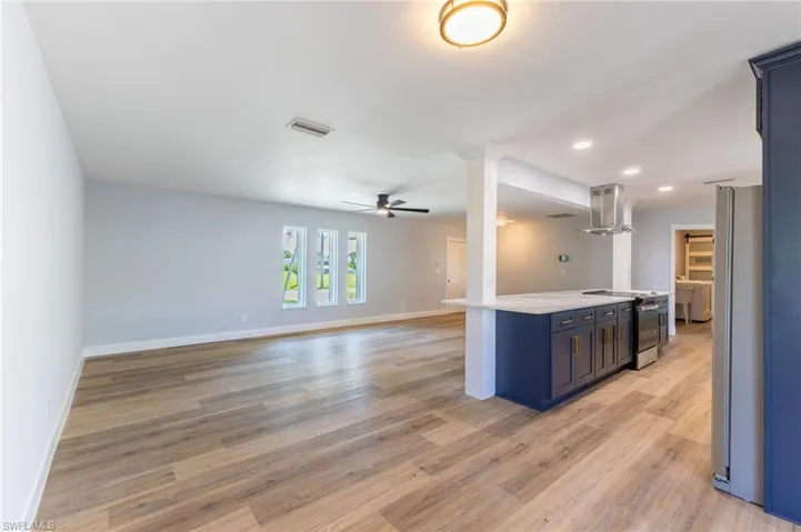 Kitchen with open floor plan, appliances with stainless steel finishes, light wood-style flooring, island exhaust hood, and light stone counters