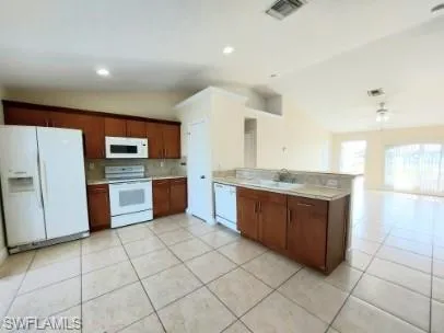 Kitchen featuring vaulted ceiling, white appliances, decorative backsplash, light countertops, and a peninsula