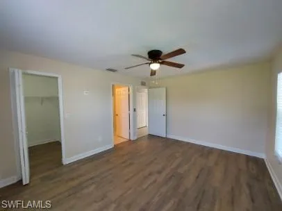 Unfurnished bedroom featuring a spacious closet, dark wood-style flooring, and ceiling fan