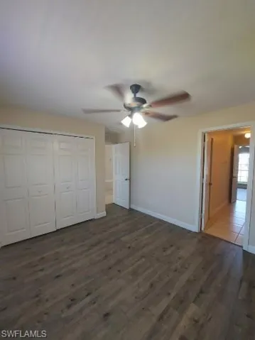 Unfurnished bedroom with dark wood-type flooring, a closet, and a ceiling fan