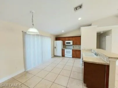 Kitchen with white appliances, pendant lighting, lofted ceiling, light tile patterned flooring, and tile countertops
