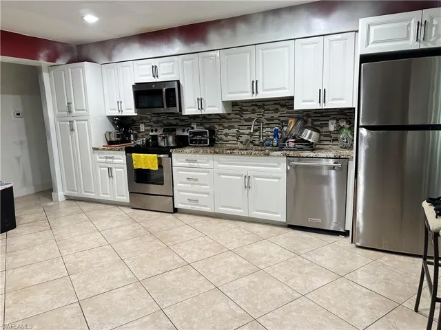 Kitchen featuring stone countertops, stainless steel appliances, backsplash, and white cabinets