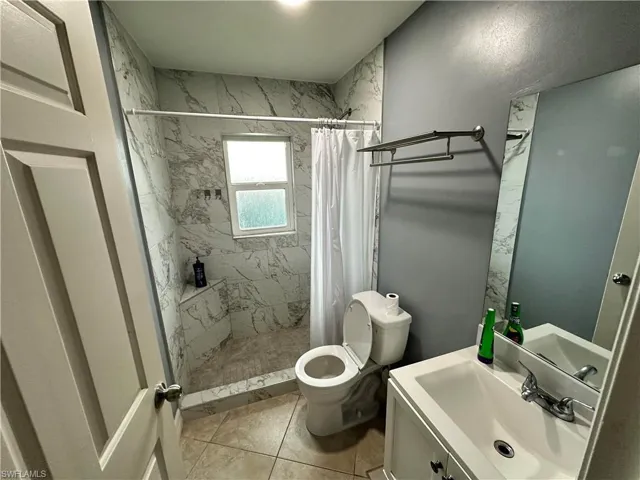 Bathroom with curtained shower, toilet, vanity, and tile patterned flooring