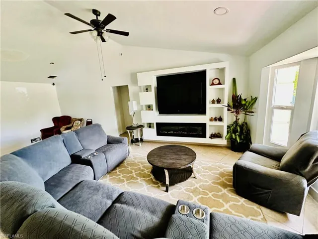 Living room featuring built in shelves, ceiling fan, lofted ceiling, and light tile patterned floors