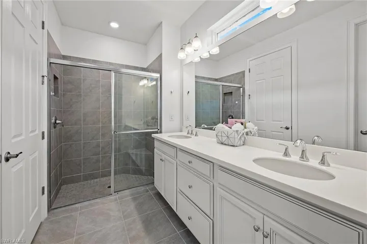 Bathroom featuring double vanity, a stall shower, and light tile patterned floors