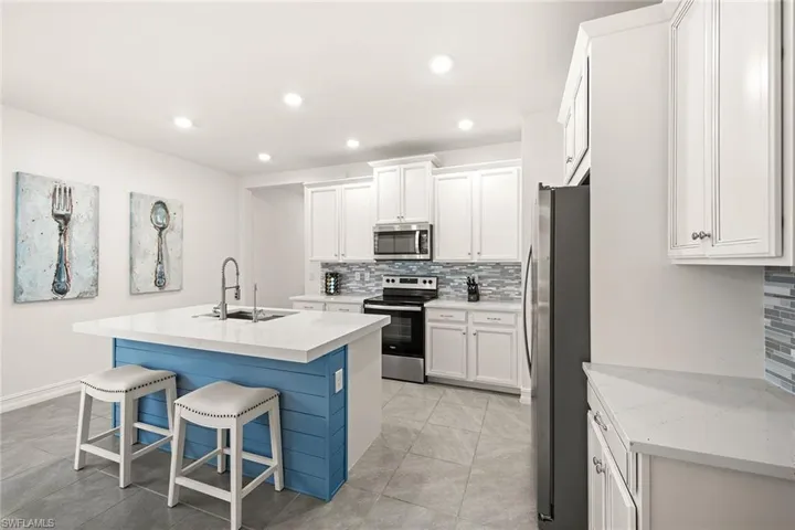 Kitchen featuring an island with sink, appliances with stainless steel finishes, tasteful backsplash, white cabinets, and recessed lighting