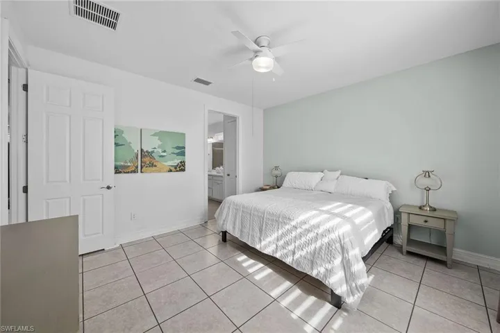 Bedroom featuring light tile patterned flooring, ensuite bath, and ceiling fan