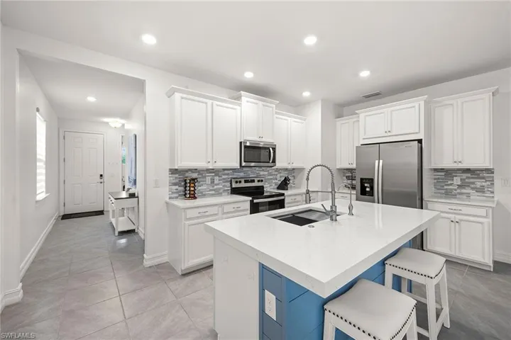 Kitchen with white cabinets, stainless steel appliances, a kitchen bar, a center island with sink, and recessed lighting