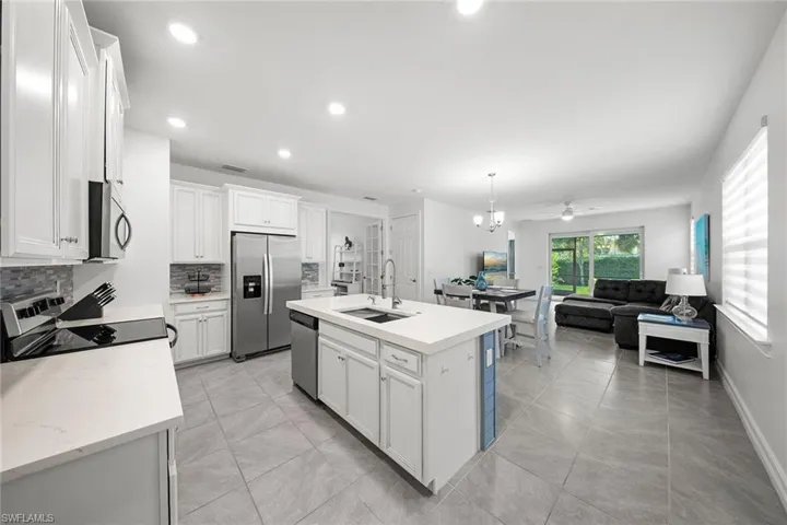 Kitchen with appliances with stainless steel finishes, a center island with sink, open floor plan, white cabinetry, and a chandelier