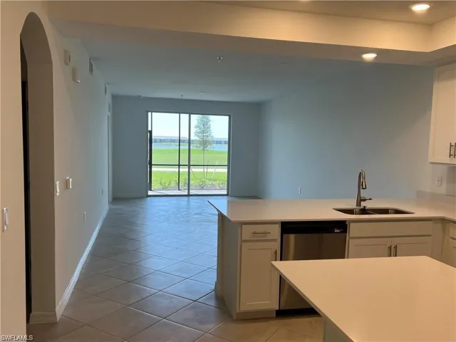 Kitchen with a peninsula, stainless steel dishwasher, white cabinetry, light tile patterned floors, and light stone countertops