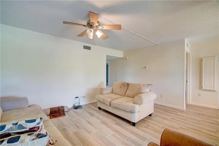 Living room with light hardwood / wood-style floors, ceiling fan, and a textured ceiling