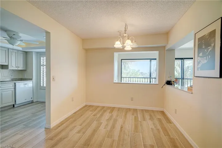 Empty room with a textured ceiling, light wood-type flooring, and ceiling fan with notable chandelier