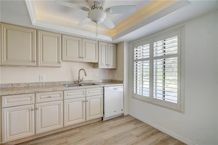 Kitchen with white dishwasher, a tray ceiling, sink, and ceiling fan