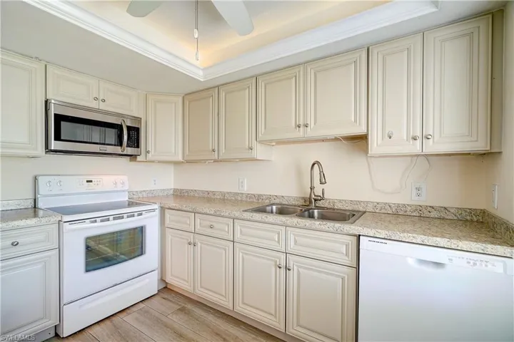 Kitchen featuring ceiling fan, a tray ceiling, light hardwood / wood-style flooring, white appliances, and sink