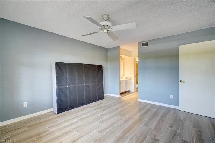 Unfurnished bedroom with ceiling fan, a textured ceiling, light wood-type flooring, and ensuite bathroom