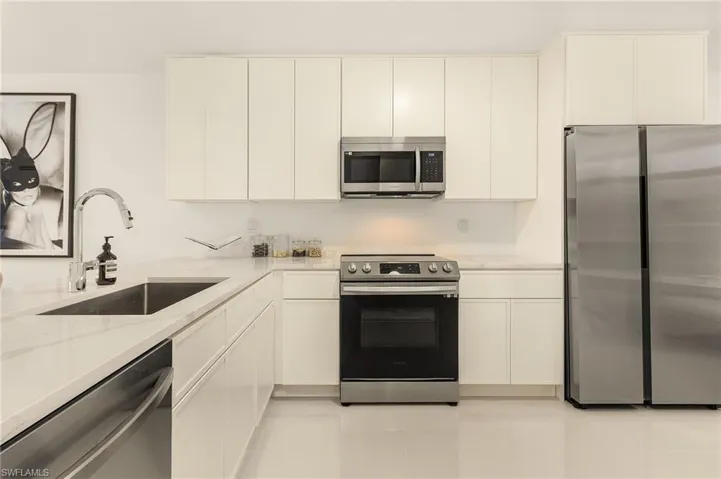 Kitchen featuring white cabinetry, light stone counters, appliances with stainless steel finishes, and a sink