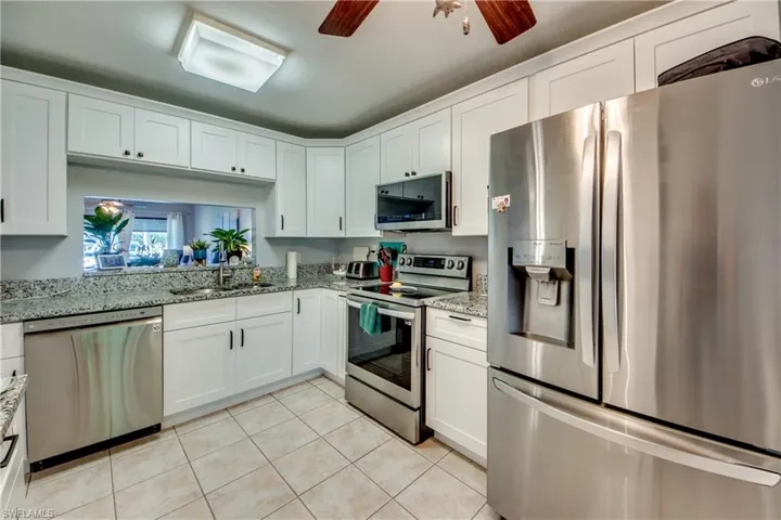 Kitchen featuring stainless steel appliances, ceiling fan, white cabinetry, light stone counters, and light tile patterned flooring
