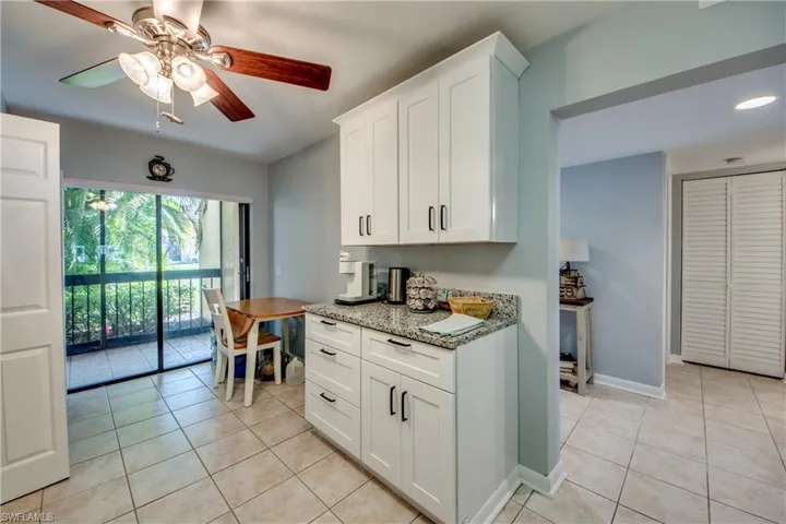 Kitchen with light stone counters, a ceiling fan, white cabinetry, and light tile patterned flooring