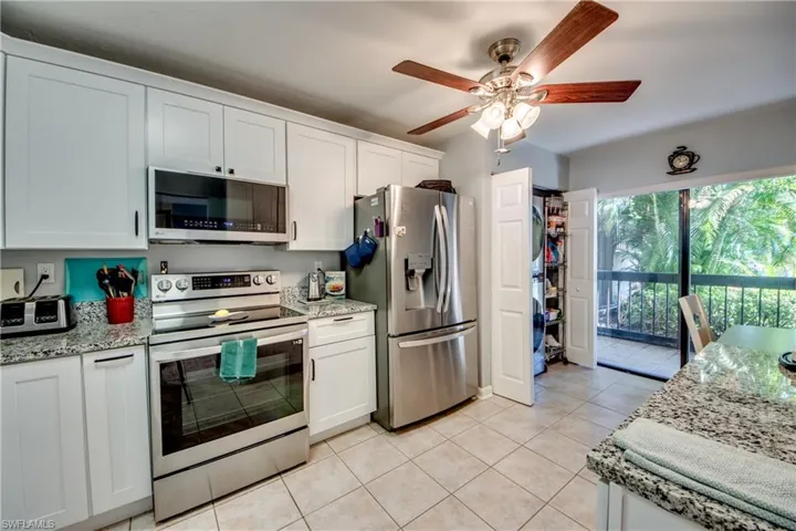 Kitchen with stainless steel appliances, white cabinetry, light stone counters, and ceiling fan