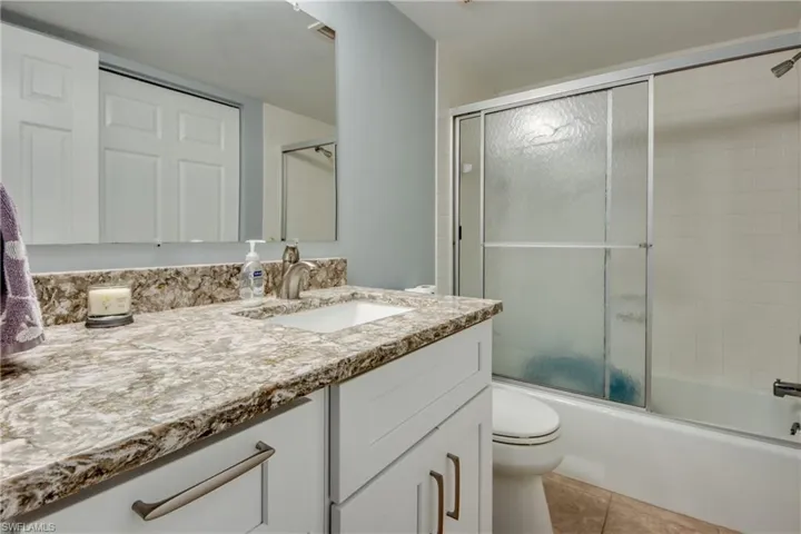 Bathroom with vanity, shower / bath combination with glass door, and light tile patterned flooring