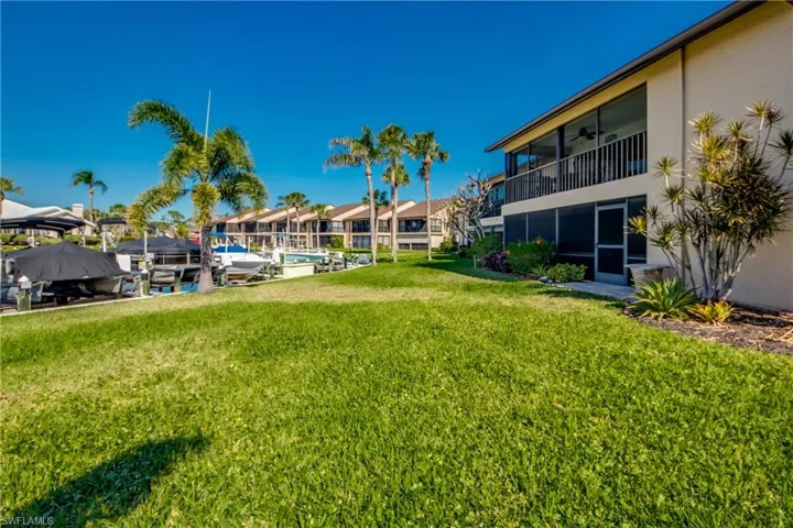 View of green lawn featuring boat lift, a dock, a sunroom, ceiling fan, and a balcony