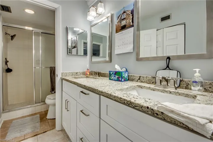 Full bath with a shower stall, double vanity, recessed lighting, and light tile patterned floors
