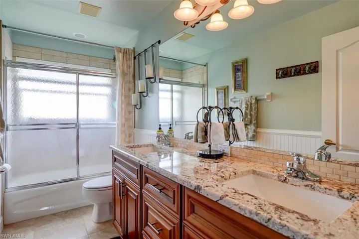 Full Guest bathroom featuring dual vanity, shower / bath combination with glass door, tile floors, and toilet
