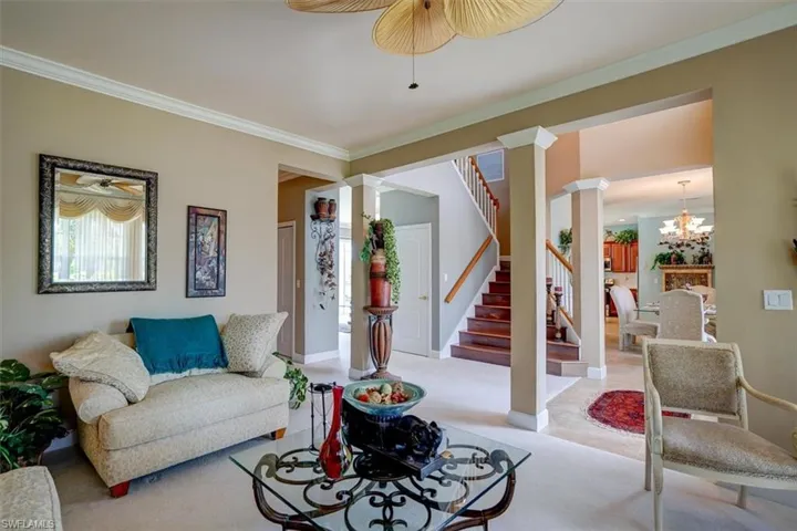 Living room featuring an inviting chandelier, ornamental molding, decorative columns, and carpet floors
