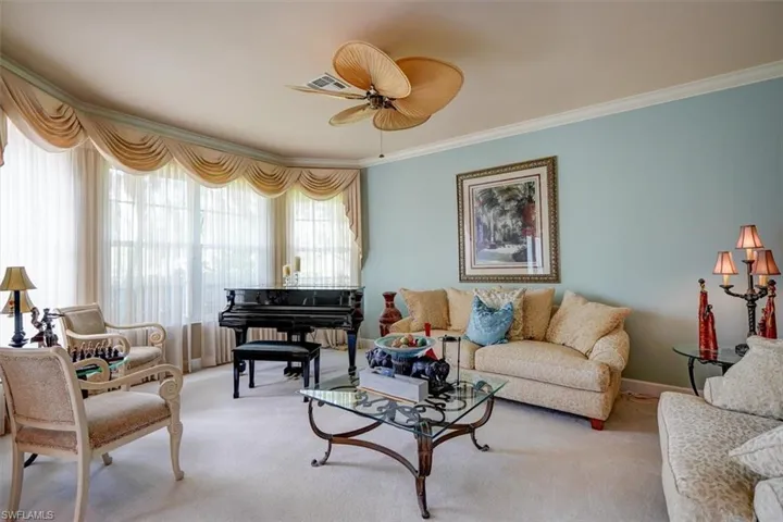 Carpeted living room with ceiling fan and crown molding