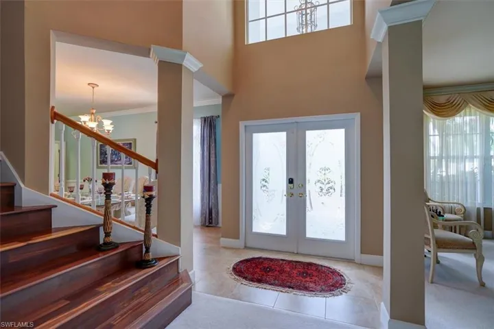 Tiled foyer with ornamental molding, french doors, an inviting chandelier, and ornate columns