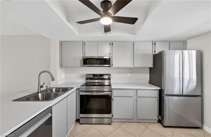 Kitchen featuring stainless steel appliances, gray cabinetry, a raised ceiling, light countertops, and a ceiling fan