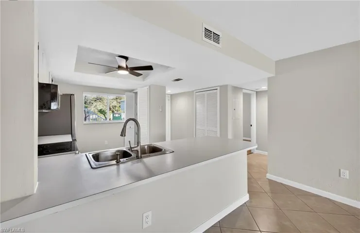Kitchen with light countertops, light tile patterned floors, ceiling fan, a peninsula, and a tray ceiling