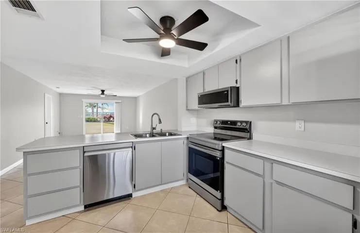 Kitchen with a tray ceiling, appliances with stainless steel finishes, gray cabinetry, and a peninsula