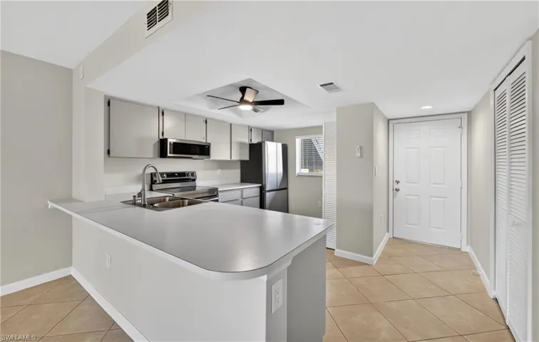 Kitchen with appliances with stainless steel finishes, a peninsula, light tile patterned floors, and light countertops