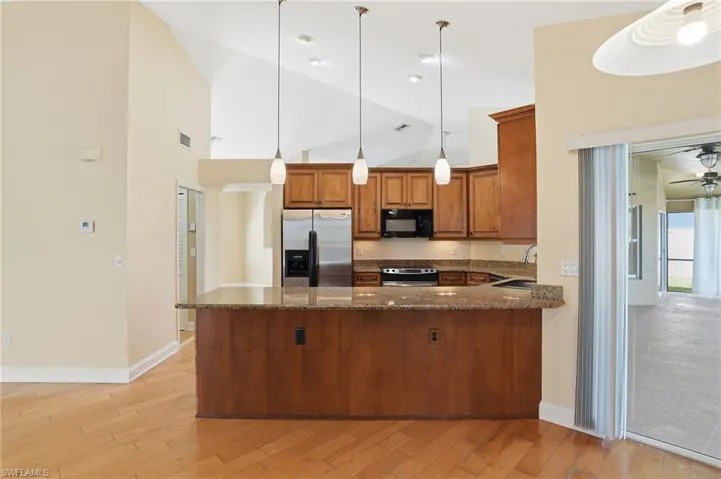 Kitchen featuring wood finish cabinets, dark stone counters, stainless steel appliances, light wood-type flooring, and pendant lighting