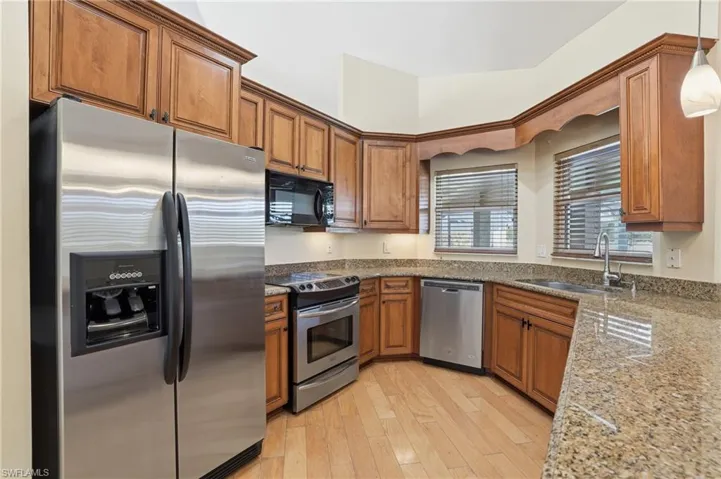 Kitchen featuring stainless steel appliances, wood finish cabinetry, light stone counters, and light wood-style floors