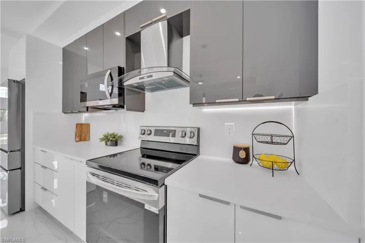 Sleek kitchen featuring gray and white cabinetry, a built-in microwave, stainless steel range hood, and a black electric range