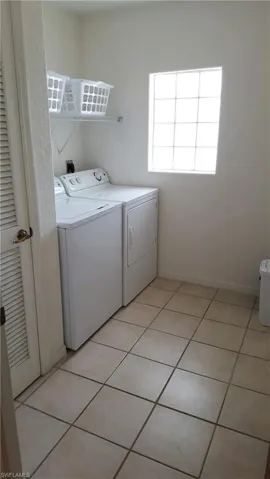 Clothes washing area featuring washing machine and dryer and light tile patterned floors