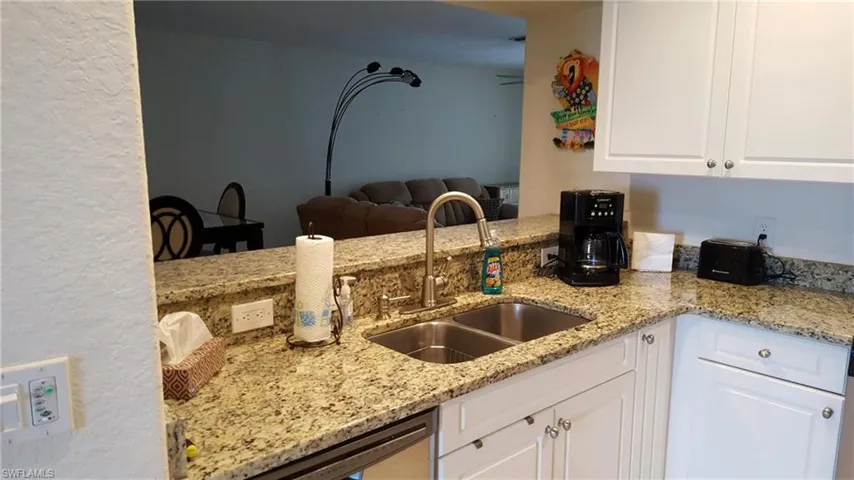Kitchen with a sink, white cabinets, light stone counters, and stainless steel dishwasher