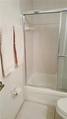 Full bathroom with toilet, enclosed tub / shower combo, and tile patterned floors