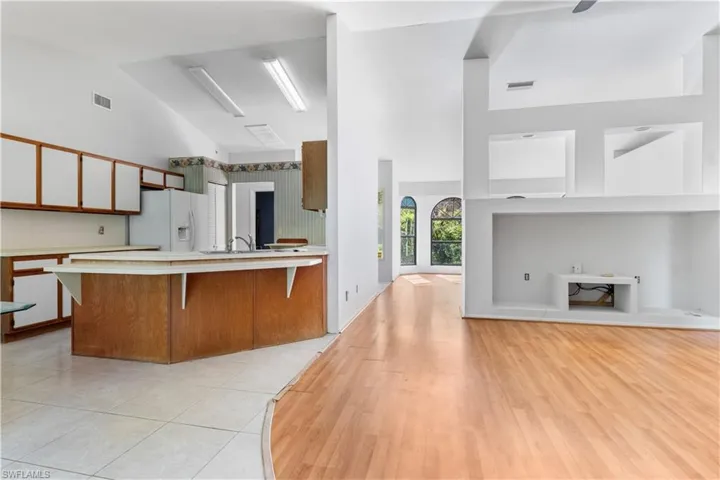 Kitchen with brown cabinetry, light countertops, a breakfast bar, high vaulted ceiling, and white refrigerator with ice dispenser