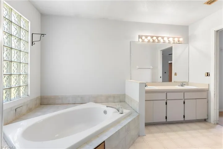 Full bathroom featuring light flooring, double vanity, and a garden tub