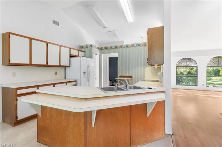 Kitchen with brown cabinetry, light countertops, white fridge with ice dispenser, white cabinetry, and wallpapered walls