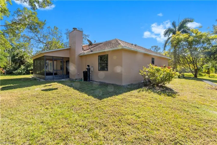 Back of property with a sunroom, a yard, stucco siding, and a chimney