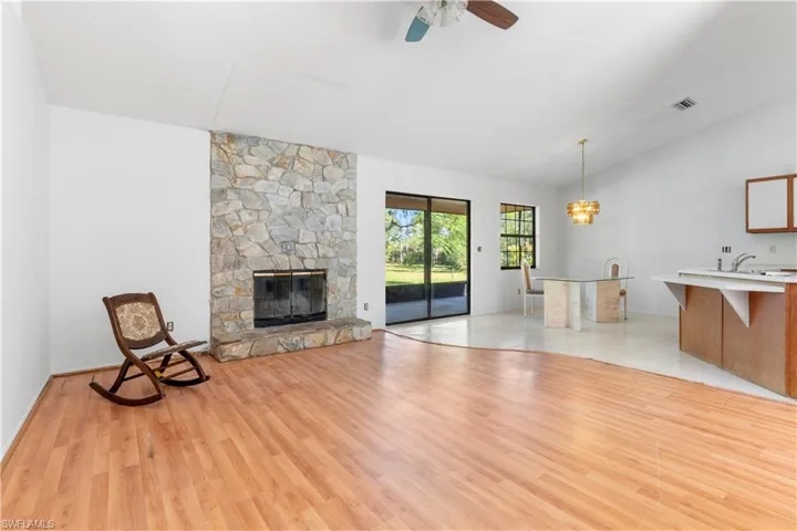 Unfurnished living room featuring lofted ceiling, light wood-type flooring, a chandelier, a stone fireplace, and ceiling fan